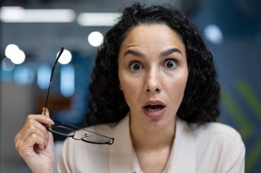 Modern ofis ortamında elinde şok edici bir ifade olan gözlüklü bir ofis çalışanı. Duygularını temsil eden profesyonel kıyafetli bir kadın. Şok, sürpriz ve beklenmedik haber kavramı.