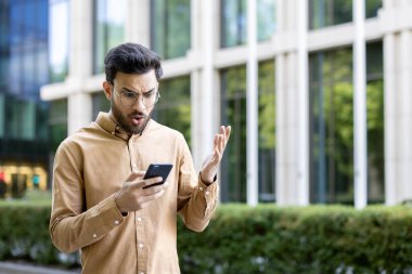 Ofis binasının dışında rahat kıyafetler giymiş bir adam hayal kırıklığıyla akıllı telefona bakıyor. Mesleki deneyim sorunu ya da haber şaşkınlık ya da öfkeye neden oluyor.
