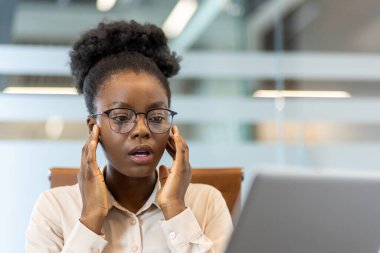Modern çalışma ortamında masa başında kötü haberler alan endişeli kadın ofis çalışanı. Çağdaş ofis ortamında çalışırken dizüstü bilgisayardaki şok edici bilgilere tepki veren gözlüklü profesyonel.