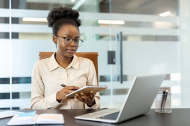 Modern ofiste çalışan iş kadınlarına odaklanmış, dizüstü bilgisayar kullanırken not defteriyle not alan, profesyonel ayarlar yapan