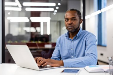 Modern ofisin içinde dizüstü bilgisayarla oturan Afro-Amerikalı iş adamı. İşadamının işe odaklandığı profesyonel bir iş yeri. Ofis kurmak üretkenlik profesyonelliğini teşvik eder.