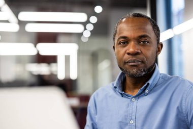 Olgun Afro-Amerikan ofis çalışanı. Parlak ışıkla modern işyerinde oturuyor. Mesleki tavır ve odaklanmış ifade verimlilik ve konsantrasyonu.