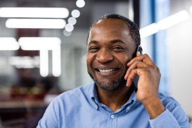 Modern ofiste gülümseyen ve telefonla konuşan bir iş adamı. Sohbet sırasında sevinç ve memnuniyeti ifade etmek. Bulanık ofis geçmişine sahip profesyonel ayar.