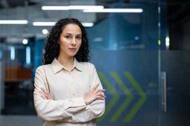 Modern ofiste kolları çapraz duran kendine güvenen bir iş kadını. Profesyonel kıyafet, modern işyeri ve kararlı ifade liderlik, güven ve profesyonelliği ifade eder..