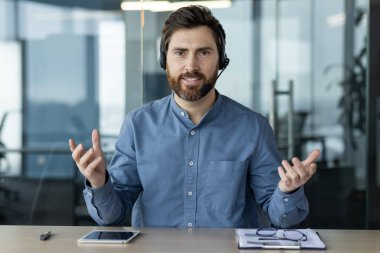 Kulaklıklı bir iş adamı modern ofis ortamında video görüşmesi yapıyor. Sanal toplantı sırasında masa başında oturan adam iletişim, teknoloji ve profesyonelliği resmediyor..