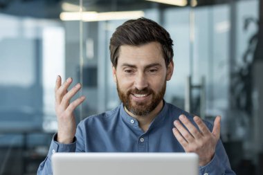 Sanal görüşme yapan kendine güvenen işadamı laptopla iletişim kuruyor. Modern ofis ortamında oturmuş, internet üzerinden profesyonel tartışmalar.