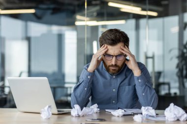 Modern ofis masasında stres ve hayal kırıklığı yaşayan bir iş adamı. Elleri, dizüstü bilgisayarı ve buruşuk kağıtları olan, zorlu bir iş ortamı olduğunu gösteren bir adam. Şirket işyeri stres kavramı