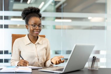 İş yerindeki bilgisayarında çalışan genç Afrikalı Amerikalı iş kadını, özgüvenle gülümsüyor. Profesyonel kadın iş ve internet iletişimi ile ilgileniyor.