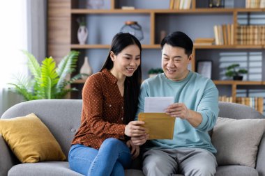 Asyalı çift rahat oturma odasında kanepede oturmuş mektuplar okuyor, gülümsüyor ve anın tadını çıkarıyorlar. Aşk kavramı, birliktelik, mutluluk ve ev