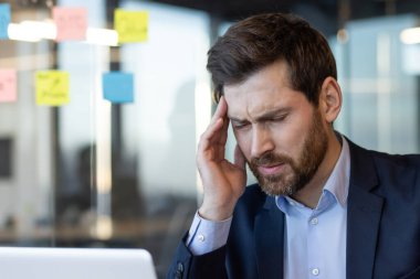 İş adamı ofiste masa başında çalışırken stresli ve dokunaklı görünüyor. Baş ağrısı, baskı ya da işle ilgili stres yaşayan bir erkek..