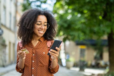 Neşeli bir kadın turist bir şehirde gezerken görülüyor, tatilin tadını çıkarıyor. Bir kredi kartı tutuyor ve cep telefonunu kullanıyor. Hem rahatlık hem de modern yaşam tarzını somutlaştırıyor..