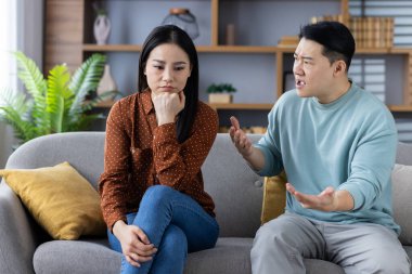 Asyalı çift kanepede tartışıyor. İlişki çatışması yaşayan eşler. Kadın üzgün görünüyor, erkek duygularını ifade ederken.