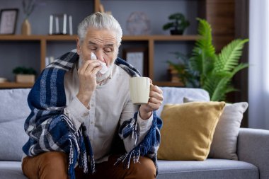 Yaşlı bir adam kendini iyi hissetmiyor, kanepede battaniyeyle kaplı bir şekilde oturuyor, elinde bir bardakla elinde içki tutuyor ve burnunu akan bir burundan peçeteyle siliyor..