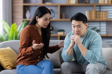 Kanepede duygusal tartışmalar yapan Asyalı bir çift. Kadın endişeli bir şekilde hareket ederken, erkek dikkatle dinliyor, düşünceli bir iletişim ve aile bağını yansıtıyor. Sahne, duygu ilişkisini aktarır