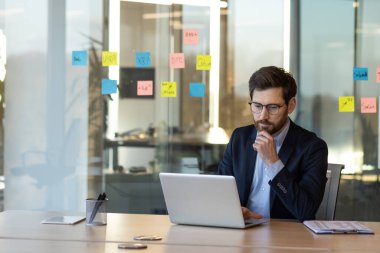 Çağdaş ofiste dizüstü bilgisayara odaklanan takım elbiseli bir iş adamı. Stratejik görevler için renkli yapışkan notlarla çevrili. İş, planlama ve teknoloji kavramları için ideal.