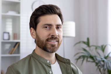 Modern ofis ortamında sakallı gülümseyen bir adam. Kendine güvenen ifadeler ve günlük giysiler profesyonel ya da yaratıcı iş yerlerini işaret ediyor.