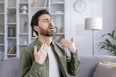 İçeriden ısı alan bir adam serinlemeye çalışırken rahatsız görünüyor. Elleriyle yüzüne doğru hareket ediyor, odadaki sıcaktan kurtulmak için..