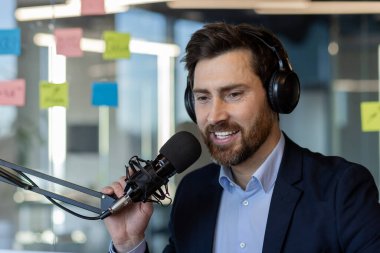 Kulaklık takan adam ofiste mikrofona konuşuyor. Yayıncılık ve podcast için ideal modern iletişim kurulumunu sağlar. Teknoloji ve iletişim üzerine odaklı profesyonel ortam.