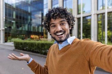 Neşeli iş adamı dışarıda selfie çekiyor, mutluluğu ve güveni ifade ediyor. Çağdaş ofis binasının yanında gülümseyerek ve rahat tavırlarla durarak..