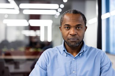 Modern ofiste odaklanmış ifadesi olan ciddi bir iş adamı. Mavi gömlek giyiyor, profesyonelliği ve bağlılığı vurguluyor. İş yeri dinamiklerini ve kurumsal ortamı vurguluyor