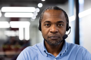 Modern ofis ortamında kulaklık takan ciddi bir iş adamı. Profesyonel çalışma ortamını vurgulayarak iletişim ve teknolojiye odaklanmış.