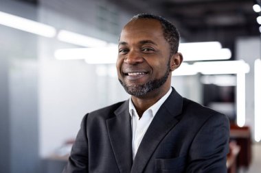 Ofis ortamında gülümseyen kendine güvenen bir iş adamı. Profesyonel takım elbiseli, beyaz gömlekli, başarılı ve liderlik timsali..