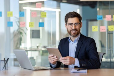 Takım elbiseli bir işadamı ve elinde tablet olan bir gözlüklü. Gülümseyen, profesyonel ve modern teknolojiyle çalışmaya odaklanmış..