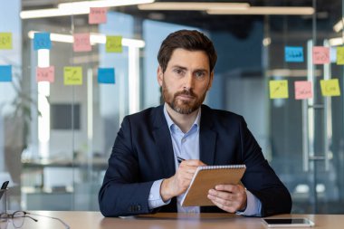 Resmi takım elbiseli kendine güvenen işadamı modern ofiste toplantı sırasında not defterine notlar yazıyor.