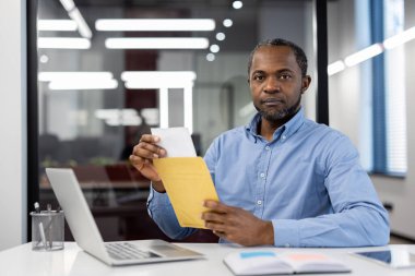 Ofis çalışanı dizüstü bilgisayar kullanırken belgeleri düzenliyor. Modern çalışma alanında verimlilik, odaklanma ve verimlilik kavramı. İşçi evrak işlerinde hassasiyet gösteriyor.