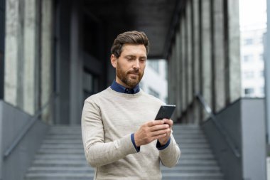 Modern ofis binasının dışında telefonu kullanan ciddi bir adam. Odaklanmayı ve teknolojiye dayalı iletişimi yansıtıyor. Mesleki, kentsel yaşamı, iş bağlantısını tasvir eden ideal resim.