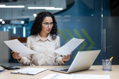 Modern ofis ortamında evrakları inceleyen ciddi ifadeli İspanyol bir iş kadını. İş analizi ve karar verme kavramı.