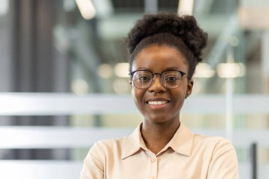 Ofis ortamında gülümseyen kendinden emin Afrikalı Amerikalı iş kadını. Gözlük takarak profesyonelliği, liderliği ve kurumsal çevrede başarıyı temsil ediyor..