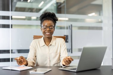 Ofis masasında oturan Afrikalı Amerikalı iş kadını meditasyon pratiği yapıyordu. Kadın, iş ortamında farkındalık göstermek için dizüstü bilgisayar ve akıllı telefon kullanıyor.