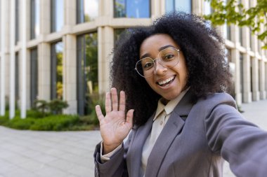 Kendine güvenen Afro-Amerikalı iş kadını telefon görüşmesinde el sallıyor. Çağdaş ofis binasının önünde duruyor. Mesleki ve dostane tavırlar iş iletişimini geliştirir.