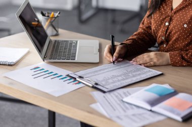 Finansörün elleri yakın plan, evrak işlerinde çalışan kadın muhasebeci, formları doldurur ve verileri formlara doldurur, mali raporları uzlaştırır, hesap makinesi ve dizüstü bilgisayar kullanır, uzlaşma sonuçları yazar.