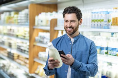 Marketteki adam akıllı telefon kullanırken elinde bir şişe süt tutuyor. Mandıra bölümünde telefonla müşteri alışverişi, teknoloji ile ürünleri karşılaştırma.