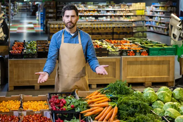 Kendine güveni tam bir market çalışanı taze sebzelerle dolu bir bölümde duruyor. Havuç, turp, vişne domatesli işçinin canlı renkleri..
