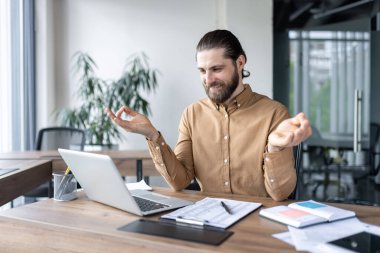 İş adamı teneffüste online yoga seansına katıldı. Dizüstü bilgisayarla masaya oturmuş, iş ve sağlık arasındaki dengeyi koruyor. Ofiste farkındalık stres yönetimi kavramını sembolize eder.