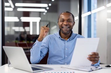 Olgun Afro-Amerikan iş adamı ofis ortamında mutluluk ve başarıyı ifade ediyor. Dizüstü bilgisayar kullanan bir adam. Profesyonel başarı kavramı, kurumsal kültürde motivasyon.