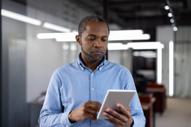 Modern ofiste tablet kullanan Afro-Amerikalı olgun iş adamı. Üretkenlik ve konsantrasyon gösteren teknolojiyle ilgilenen profesyonel biri. Liderliği vurgulayan iş kavramı