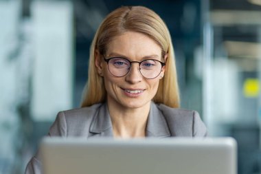 Gözlük takan kendine güvenen iş kadını modern ofiste dizüstü bilgisayarla çalışmaya odaklandı. Dijital çalışma ortamı ile uğraşırken profesyonelliği ve konsantrasyonu gösterir