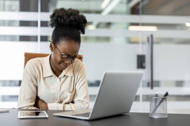 İş yerindeki genç Afro-Amerikalı kadın dizüstü bilgisayarı ve telefonu ile mide ağrısı çekiyor. Ofis ortamında kadın profesyonel çalışırken rahatsızlıkla başa çıkıyor.