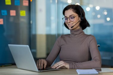 Ofis ortamında dizüstü bilgisayarla çalışan kulaklık takan profesyonel bir kadın. Modern teknolojiyi kullanarak uzaktan çalışma ve iletişimle meşgul oldu..