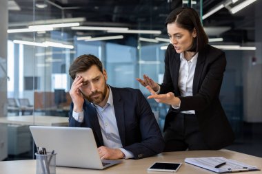 Çelişkili ofis sahnesinde kızgın bir bayan patronun hayal kırıklığına uğramış bir erkek çalışana bağırdığı görülüyor. İş görüşmelerinde gerginlik işyeri stresi ve baskısını vurguluyor.