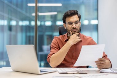 Gıcır gıcır ofisindeki girişimci masadaki bilgisayar ve telefonla belgeleri inceliyor. Çevre, odaklanma, konsantrasyon ve profesyonel iş analizi becerilerini gözler önüne serer