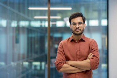 Modern ofis içinde ciddi ifadeleri olan genç bir profesyonel. İş kıyafetleri iş yeri güvenini gösteriyor. Girişimcilik, liderlik ve kurumsal çevre konuları için ideal.