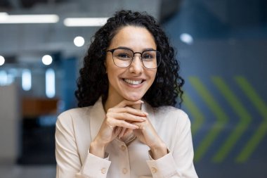 Modern ofis ortamında kameraya güvenle gülümseyen mutlu profesyonel kadın. Pozitiflik, bağlantı ve profesyonel iletişim becerilerinin portrelenmesi