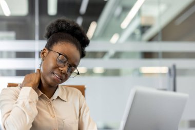 Ofis çalışanı stresli ve rahatsız görünüyor, dizüstü bilgisayar kullanırken boyun ağrısı çekiyor. Sahne, iş yerinde stres, rahatsızlık ve ergonomik farkındalık ihtiyacını taşır.