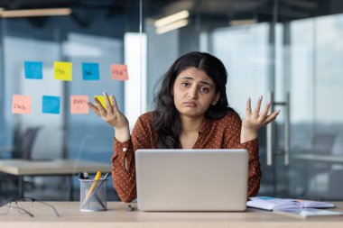 Ofis çalışanı modern çalışma ortamında hayal kırıklığına uğramış ve bunalmış hissediyor. Masasında dizüstü bilgisayar ve cam duvarda renkli yapışkan notlarla oturuyor. Karışıklık ve stresi gösterir, işyerindeki zorlukları temsil eder