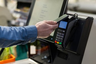 Kişi, kasadaki akıllı telefonu kullanarak ulaşılmaz ödeme yapar. Teknoloji, perakende satışlarda elverişli ve güvenli işlemler sağlıyor. Ödeme terminalinin üzerindeki el telefonuna odaklan..